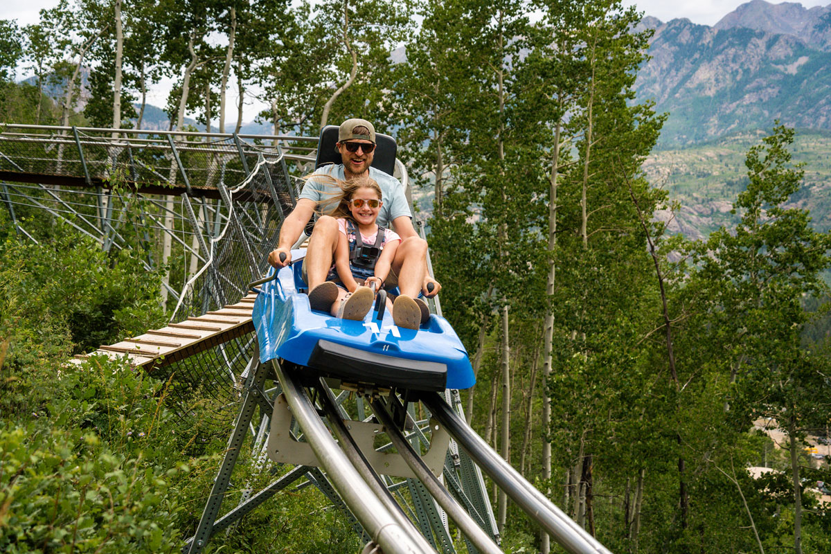 An adult and child smile as they descend the Inferno Mountain Coaster at Purgatory Resort.