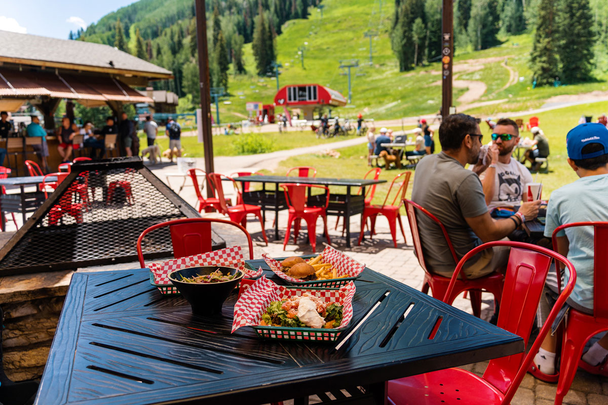 Outdoor dining area at Purgatory Resort with meals on a patio table and mountain bike trails visible in the background.