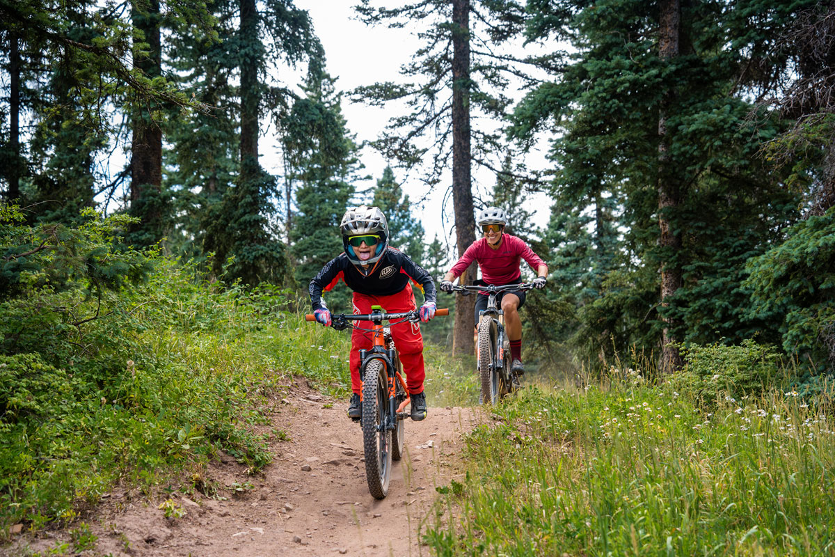 A child and adult ride mountain bikes along a wooded singletrack trail at Purgatory Bike Park.