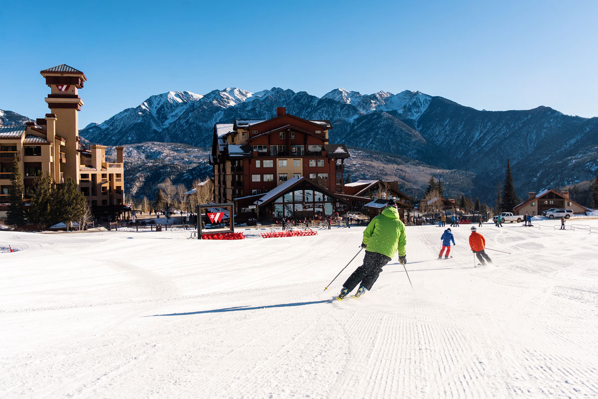 Skiers carve across freshly groomed trails at Purgatory Resort, framed by lodges and the San Juan Mountains.