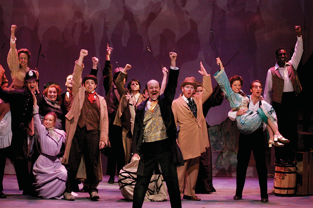 An ensamble of performers dressed in old-fashion clothing hold their arms in the air onstage at the Creede Repertory Theatre