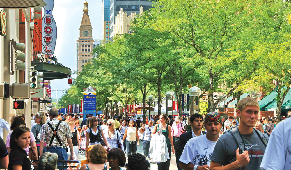 People walk down the street of Denver's 16th Street Mall on a sunny day with a bright green tree in the background