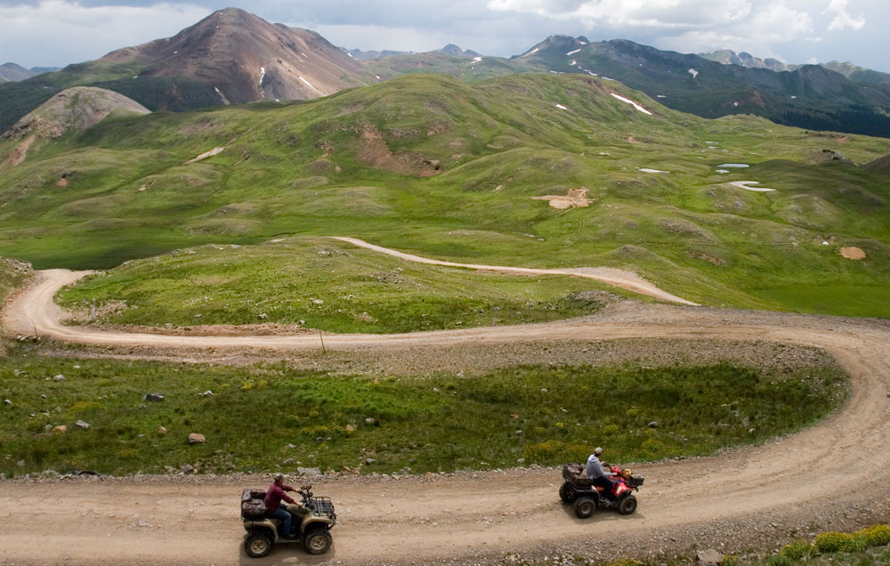 Two ATV riders follow a winding dirt track on Engineer Pass near Ouray, Colorado.