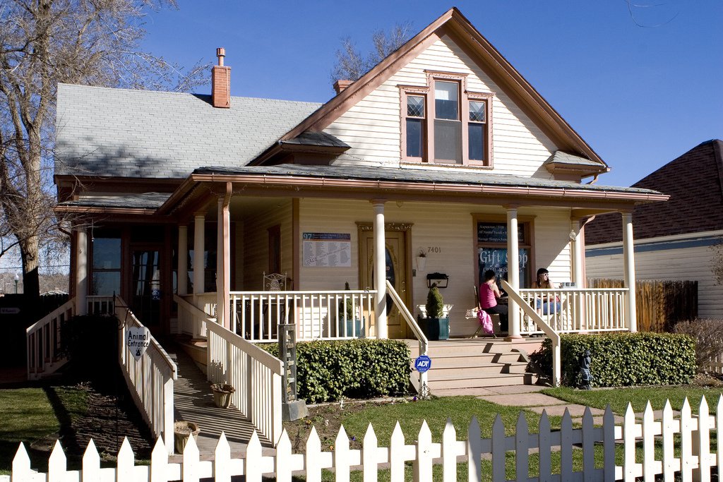 In Old Towne Arvada, an old bungalow painted yellow with a porch, front steps and a picket fence.