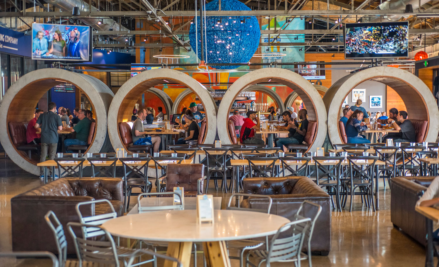 Four massive concrete cylinders set in a row act as private dining booths in a large dining space in Denver, Colorado.