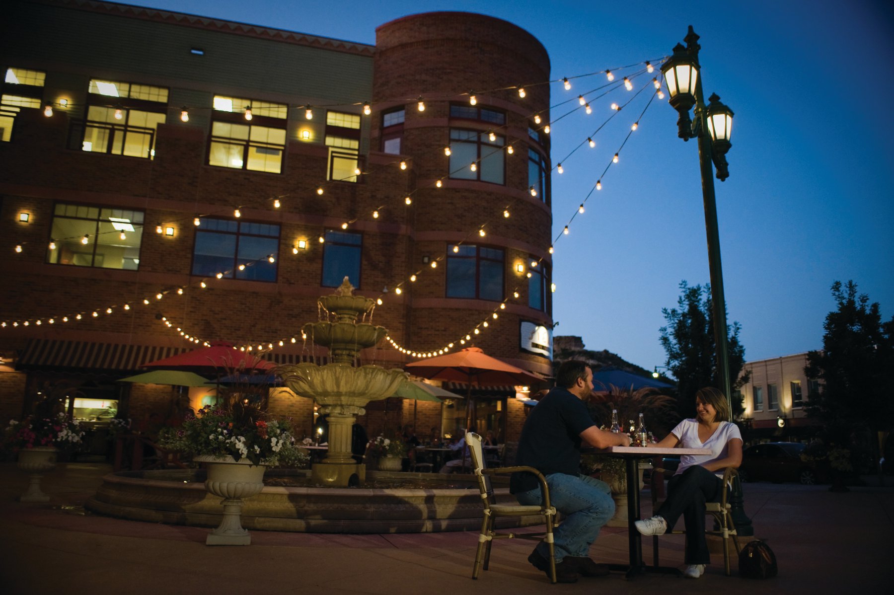 The Courtyard at night in downtown Castle Rock. A couple is having dinner and there are string light strings coming down from lights.
