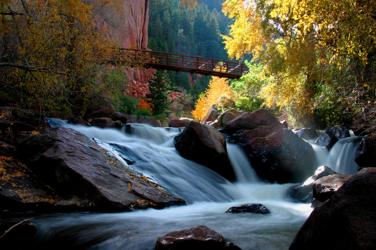 A bridge crosses high above waters cascading down piles of rocks at the Eldorado Canyon State Park in Colorado.