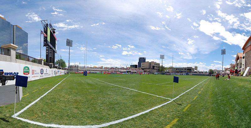 From the corner, the rugby pitch home to the Glendale Raptors on a blue-sky day. In the distance people sit on the stands.