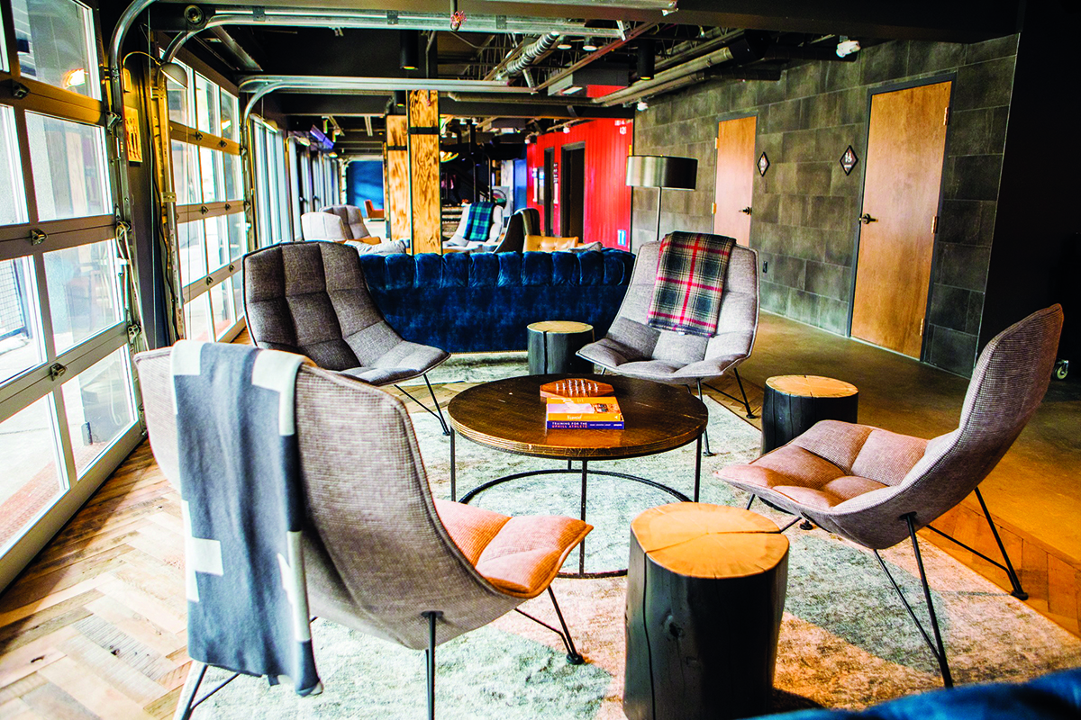 Four cozy, gray fabric lounging chairs without arm rests are arranged around a wooden coffee table at Gravity Haus in Breckenridge, Colorado.