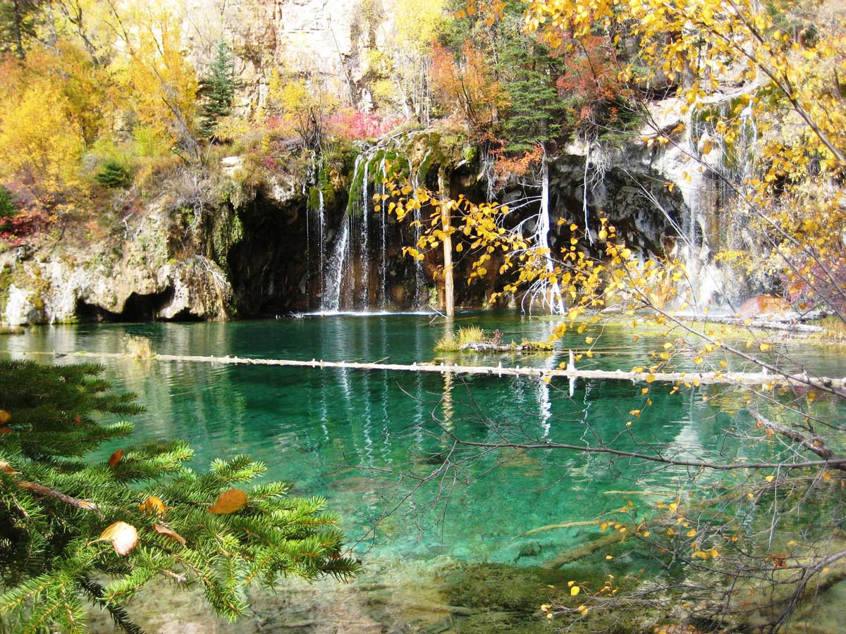 Rich fall colors of gold, orange and maroon frame a lake with transparent, green-tinged water near Glenwood Springs, Colorado.