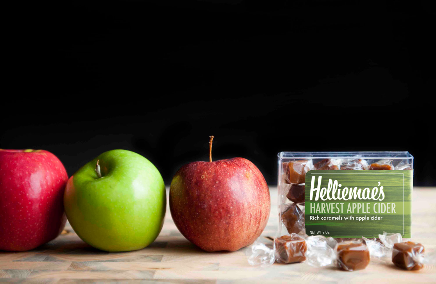 Three apples, two red and one green, are set in a row with a package of Helliemea's flavored caramel at the end in Denver, Colorado.