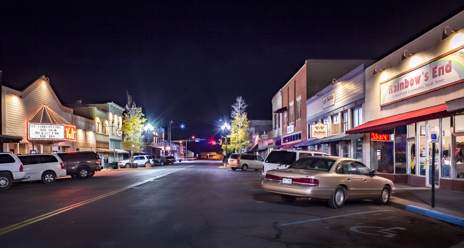 Nighttime in downtown Monte Vista with storefronts lit by the glow of streetlights with cars parked diagonally.