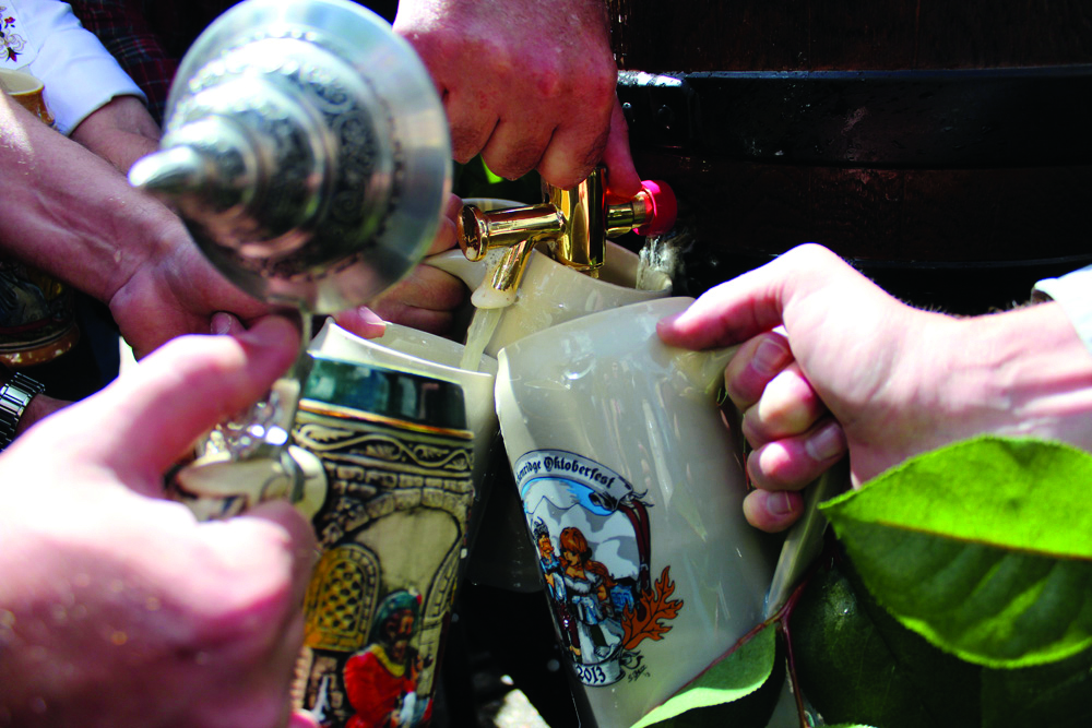Four decorative Oktoberfest beer steins are positioned around a beer keg with a gold-colored metal spigot waiting to be filled at a Colorado festival.