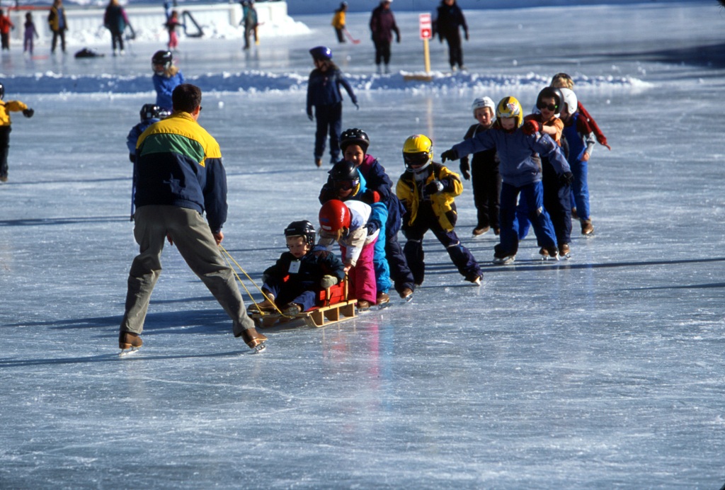 A man pulls a gaggle of children, one on a sled, the rest on ice skates across a frozen Keystone Lake.