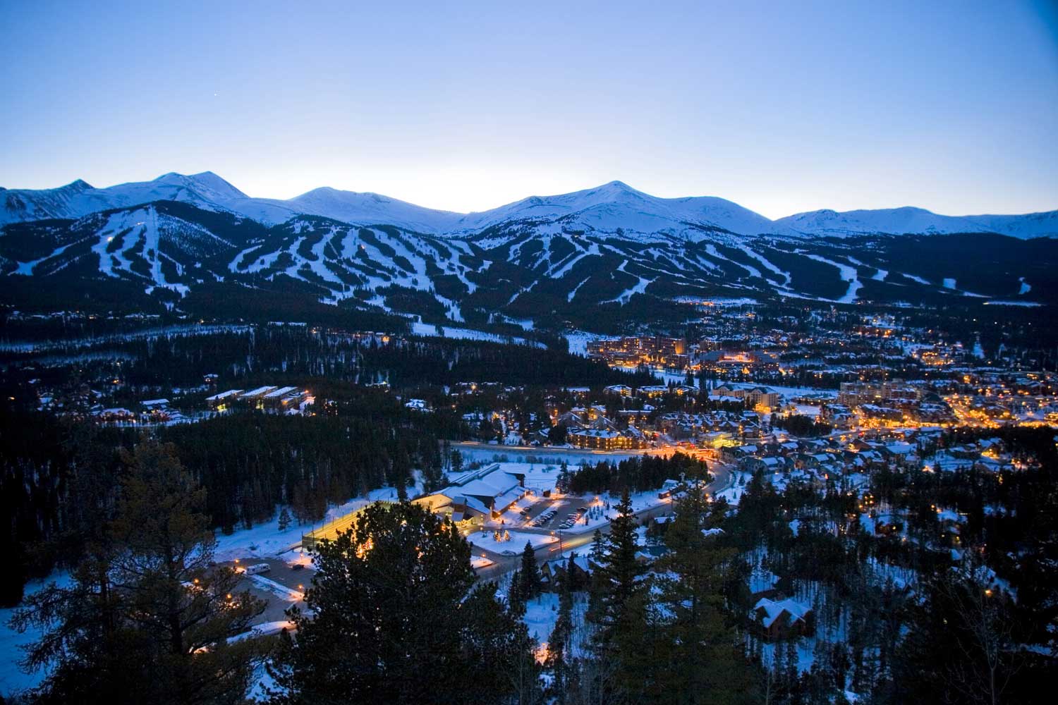 Aerial view of a mountain town lit up at night with snowy mountains in the background