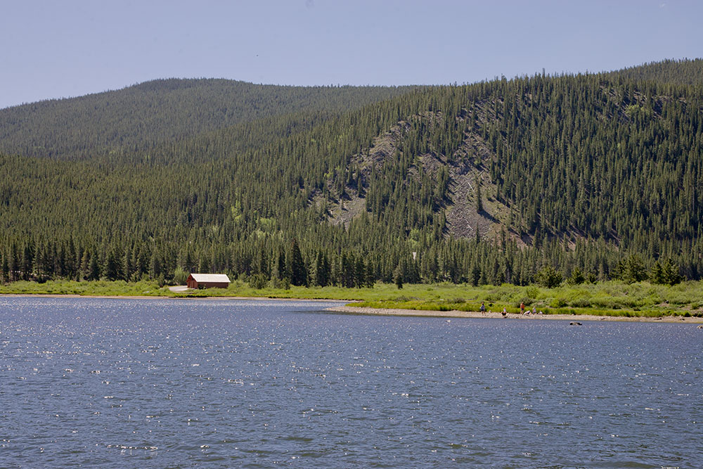The rippling blue Red Feather Lakes sit under a blue sky with grassy shores and evergreen hills.