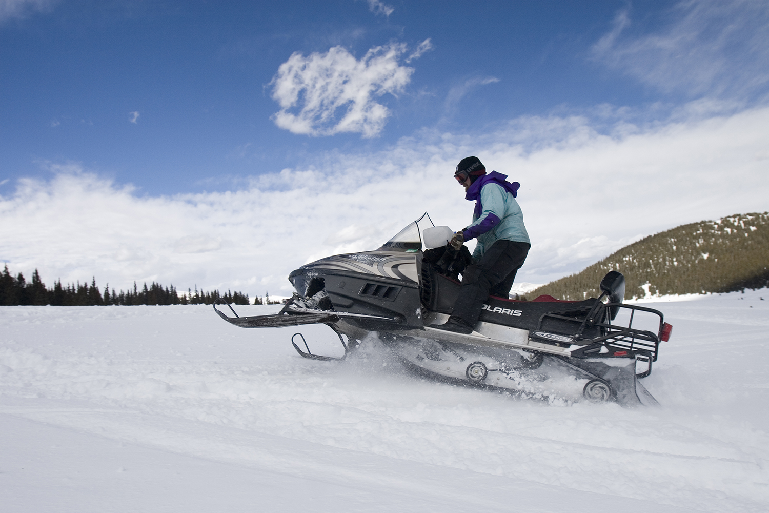 A person on a snowmobile jumps over snow bumps under a blue sky