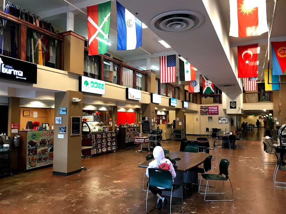 A lone diner sits at a table waiting for food at the food court at Mango House in Colorado. Above them, numerous international flags represent some of the diverse cuisines present.