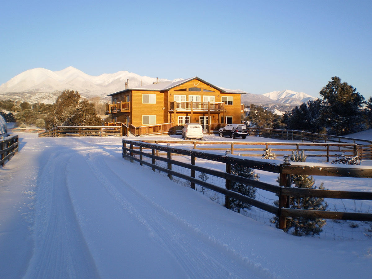 Two SUVs are parked outside a log lodge that features multiple balconies and large windows near Salida, Colorado. Behind it are tall, white mountains.
