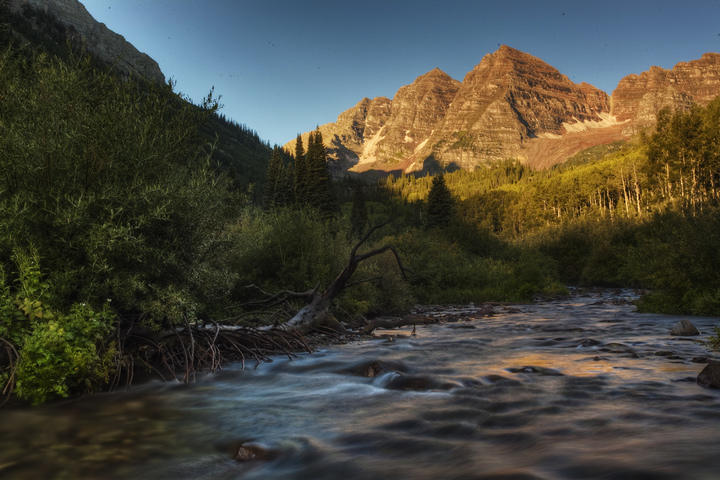 The sun shines on two mountain peaks, while in their shadow, a river runs through it