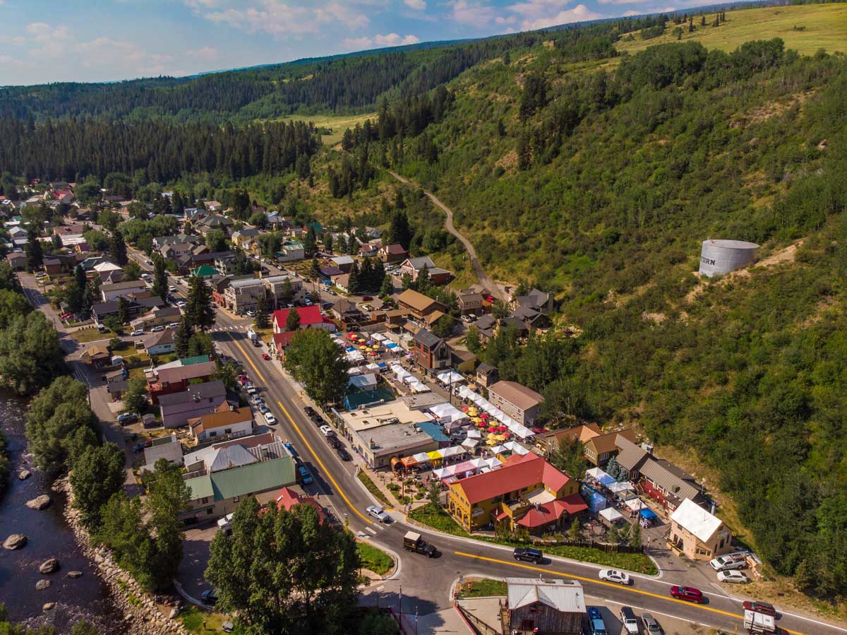 An aerial view of the town of Minturn. On the left is a river with boulders in it. On the right is a green tree and bush cover mountain.