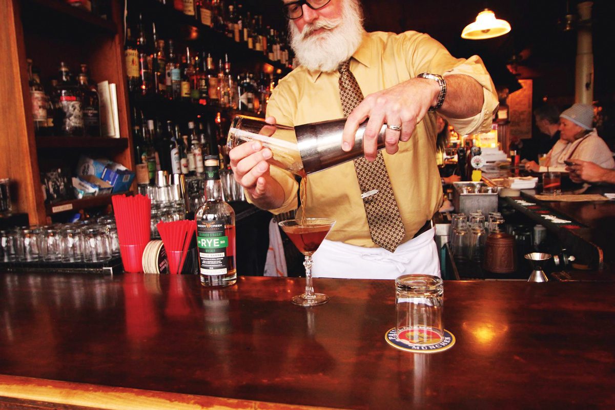 A bartender shaking and pouring cocktails into glasses