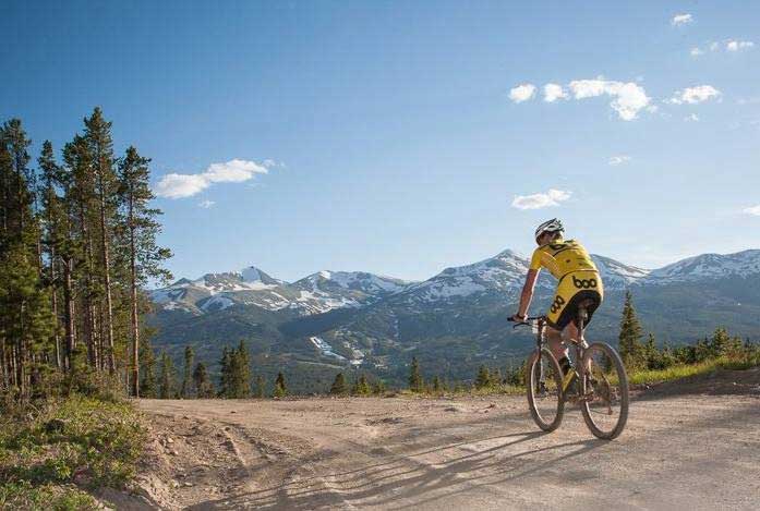 A cyclist in vibrant yellow biking clothes rides on a wide dirt road near Breckenridge, Colorado. 