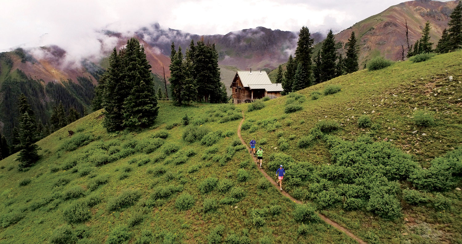 Three people run on a narrow trail leading to the OPUS Hut outside Silverton.