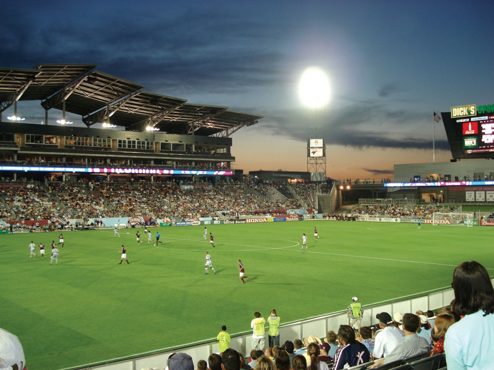 The stadium lights brighten the green soccer field while two tiers of fans fill up the stands to watch two teams play