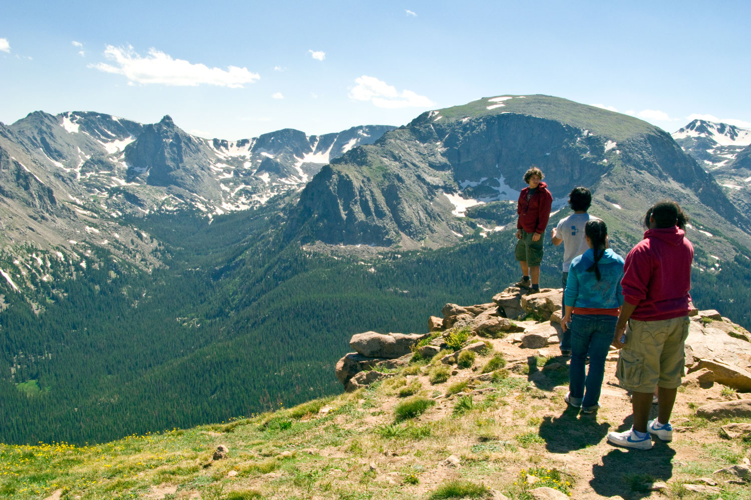 A group of hikers stop at a rocky outcropping to admire the view of the forested valley below in Rocky Mountain National Park.