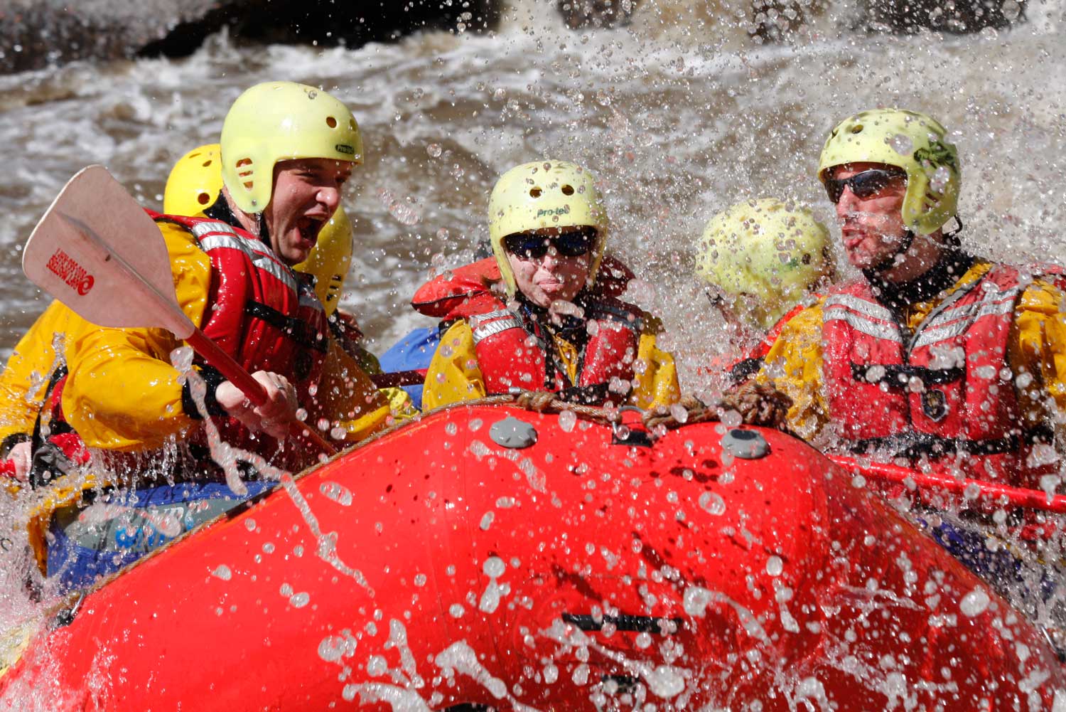 A group in helmets splashes down the river on a red raft