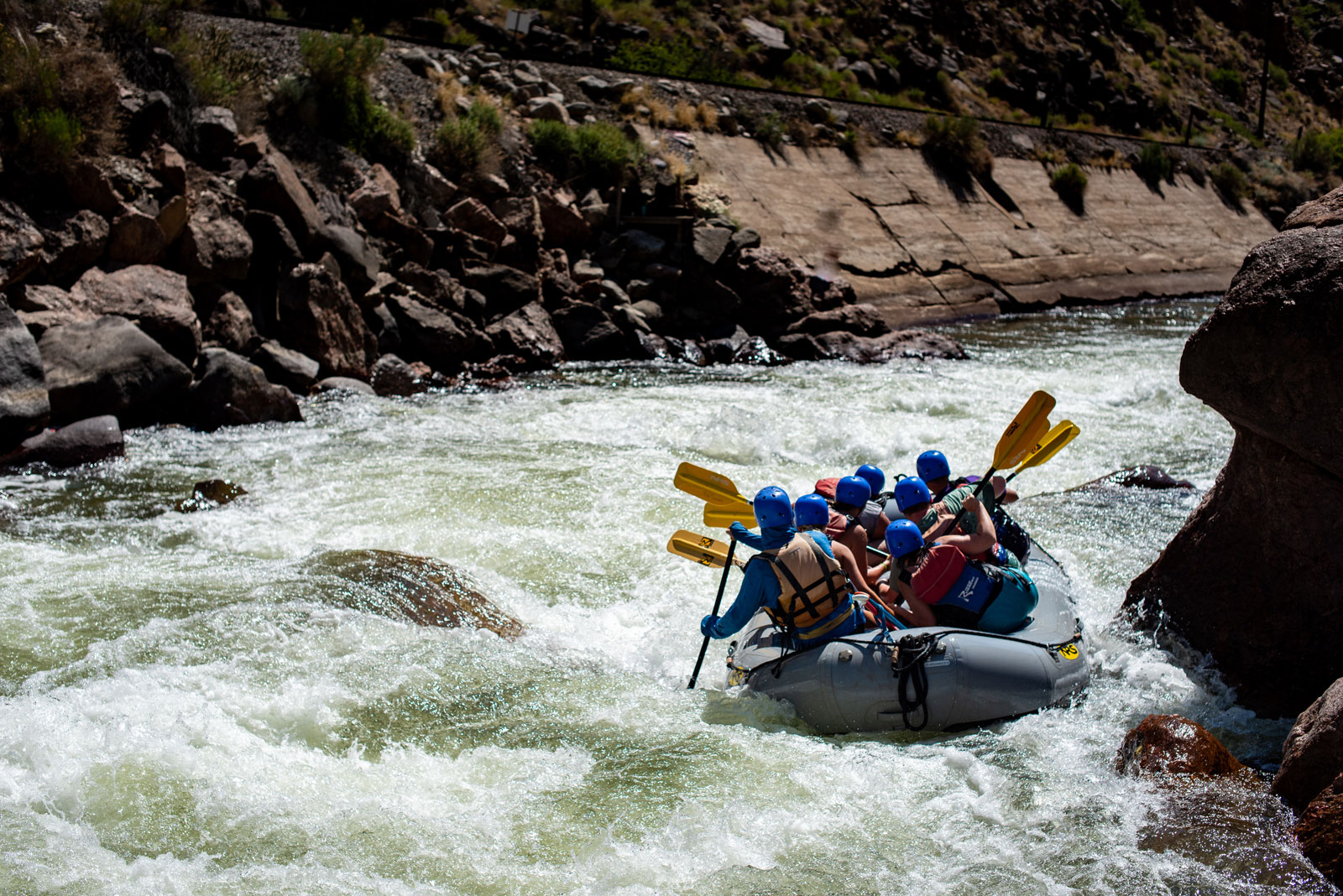 A raft of paddlers steers around a giant rock in the middle of the river