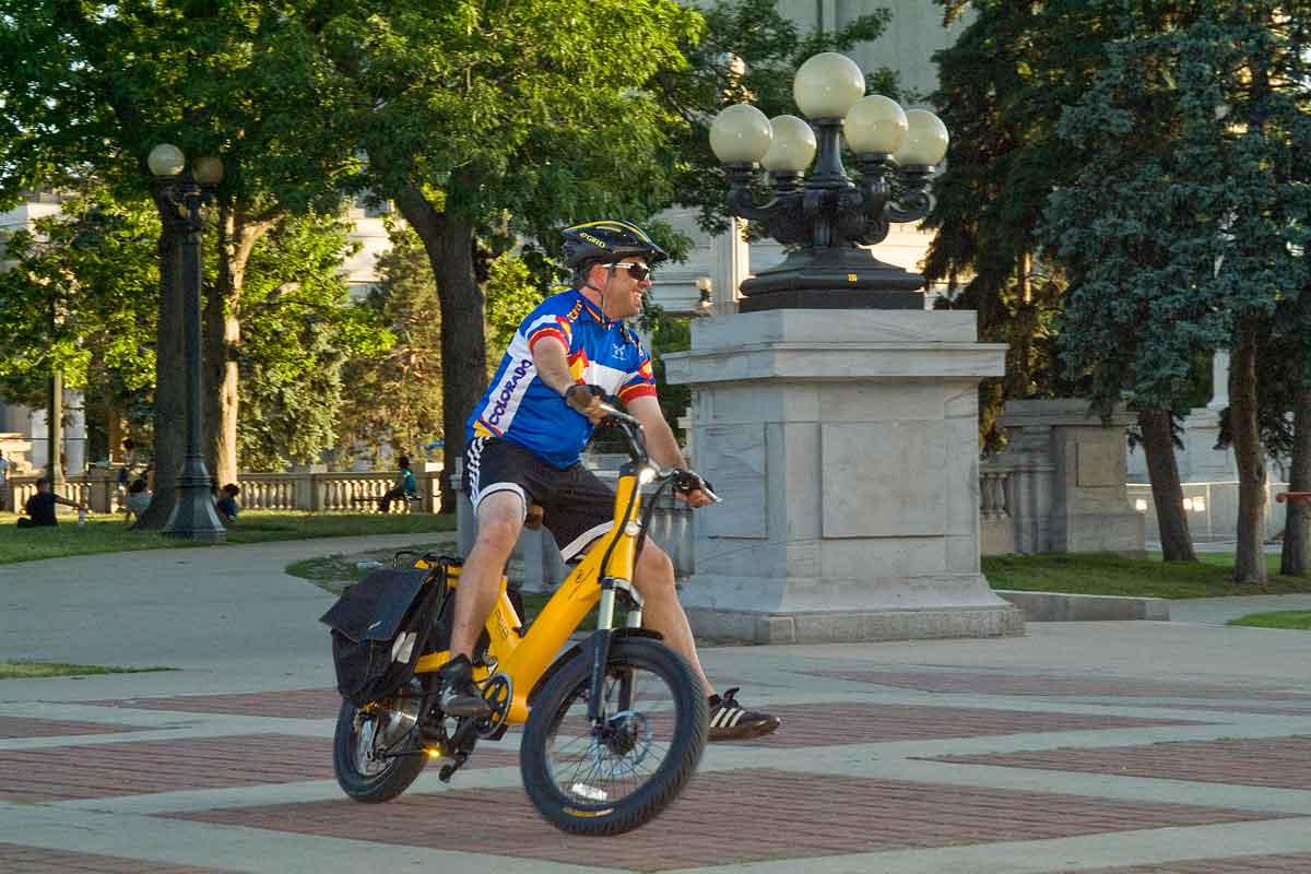 A man on a yellow E-Bike zooming around the Colorado State Capitol in Denver