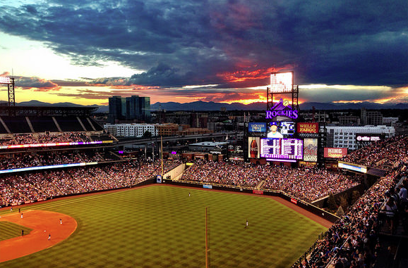 The sun sets behind a baseball field lit up at night