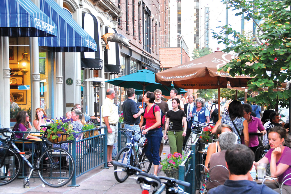 A crowd of people is shown eating and shopping on a busy downtown street