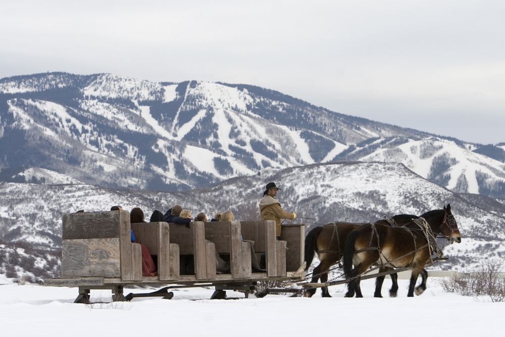 A group of people enjoy a sleigh ride with snowy mountains in the background
