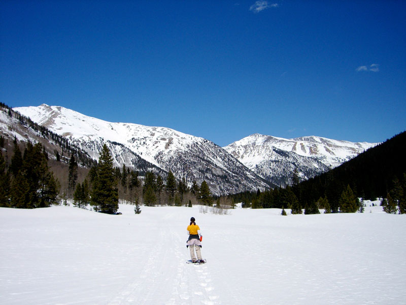 A lone snowshoer makes tracks in a valley with large mountains in the background