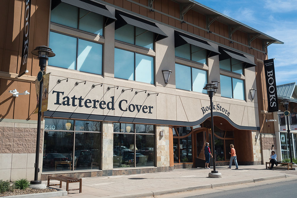 A brown and tan store front says "Tattered Cover" on the right side of the building and above the door it says "BookStore." 