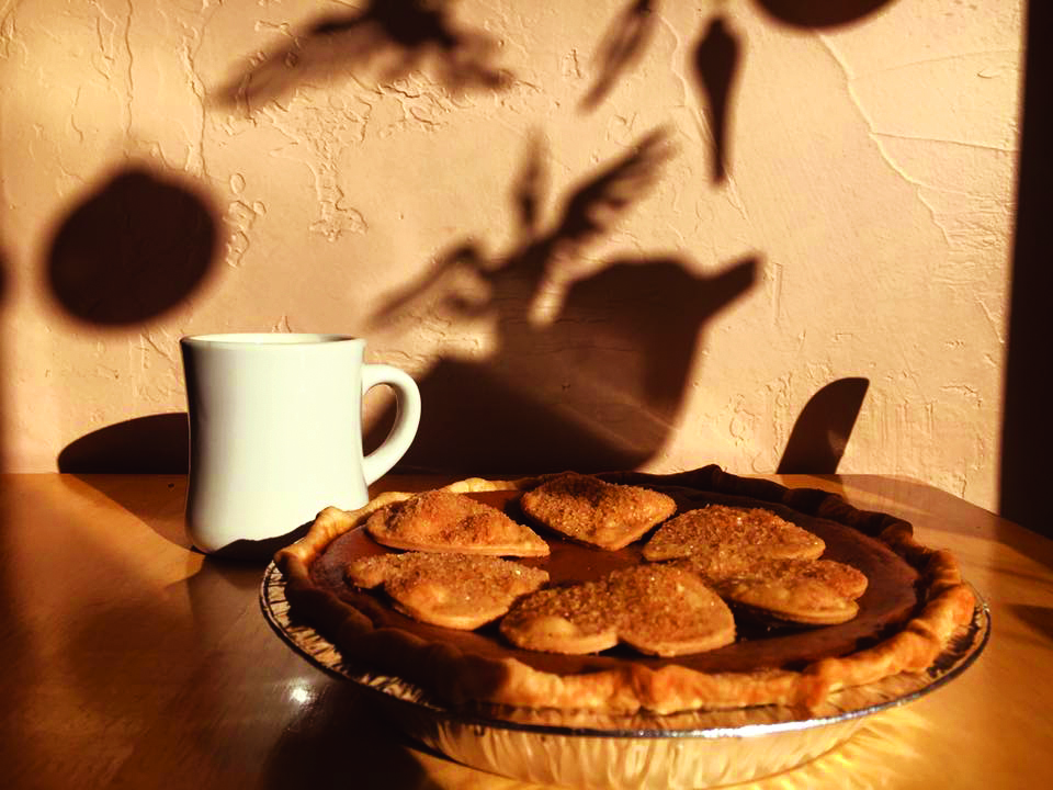 A white ceramic coffee mug sits on a table next two a freshly baked pie at the Pie Maker Bakery in Cortez, Colorado. Atop the pie are sugared heart-shaped crust pieces.