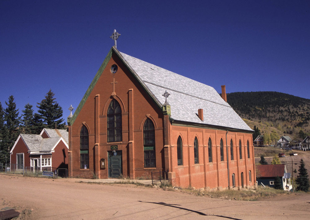 The Richardson-Romanesque St. Victor's Catholic Church sits on a dirt road with a deep-blue sky up above.