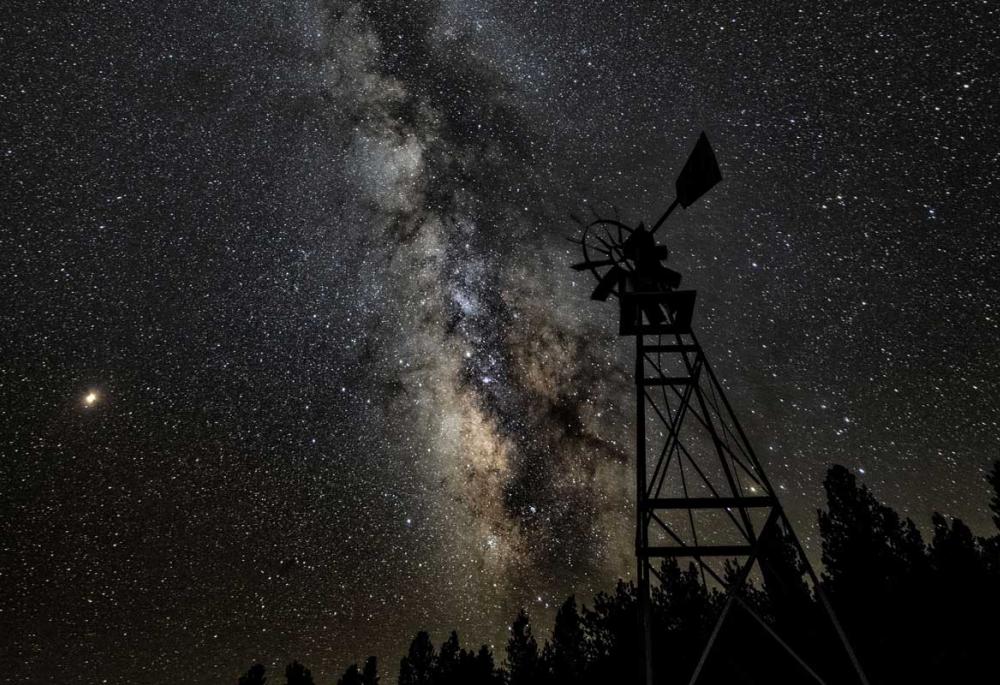 An old-school windmill with a view of the Milky Way and the night sky's stars.