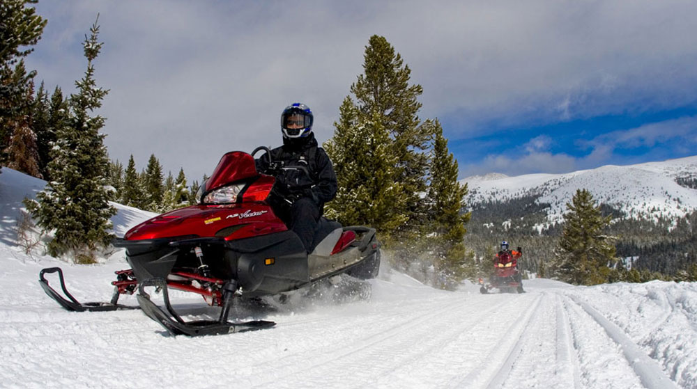 A person in a red snowmobile steers his sled along a snowy trail