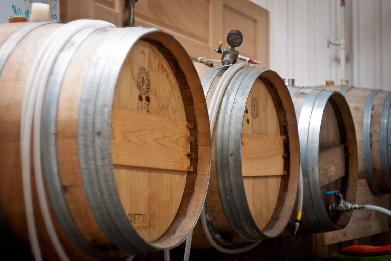 Light-wood casks of whiskey sit on their sides a shelf in a whiskey distillery in Denver, Colorado. The barrels are hooked up to hoses.