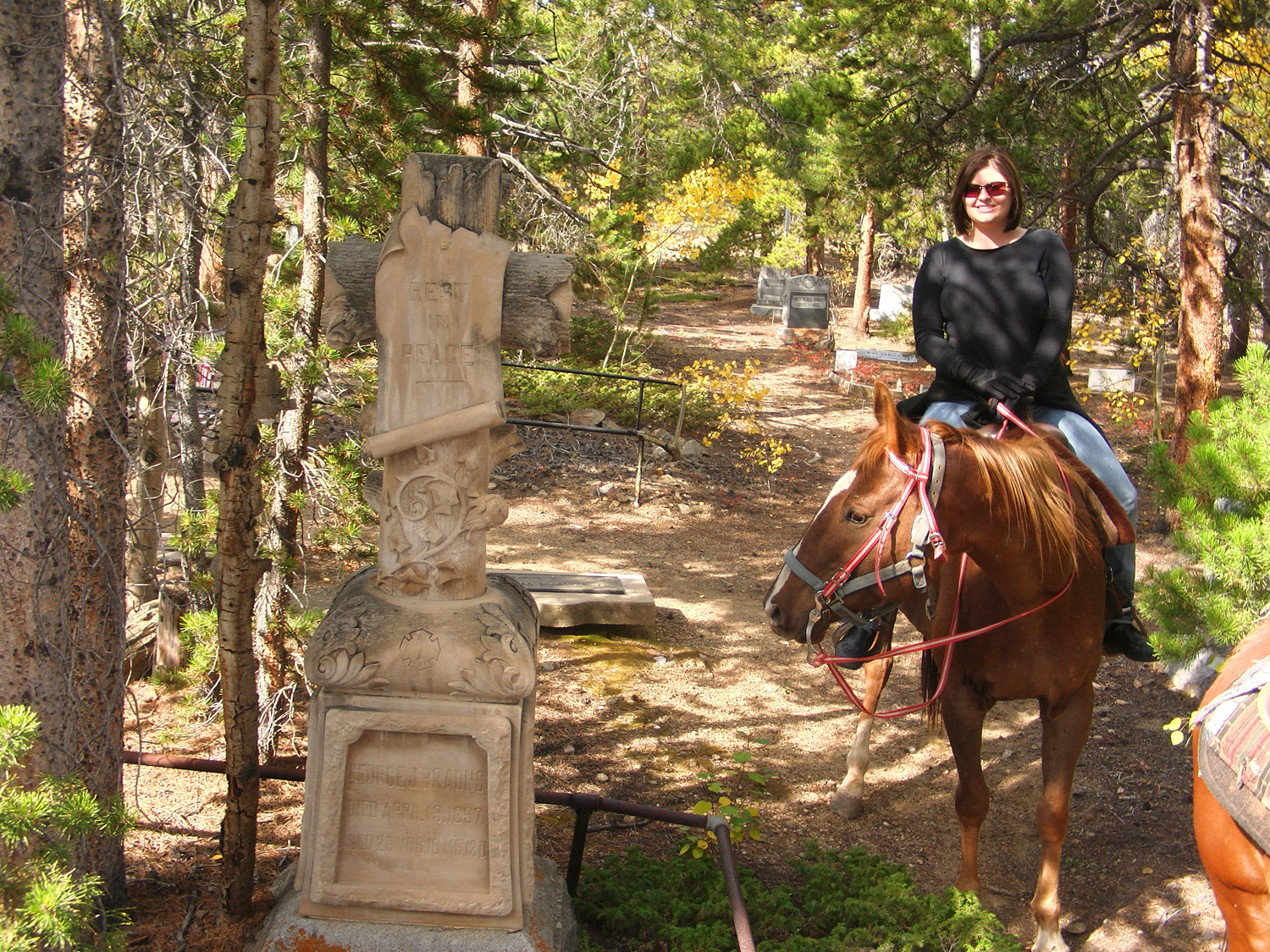 A woman on horsed rides through a wooded trail