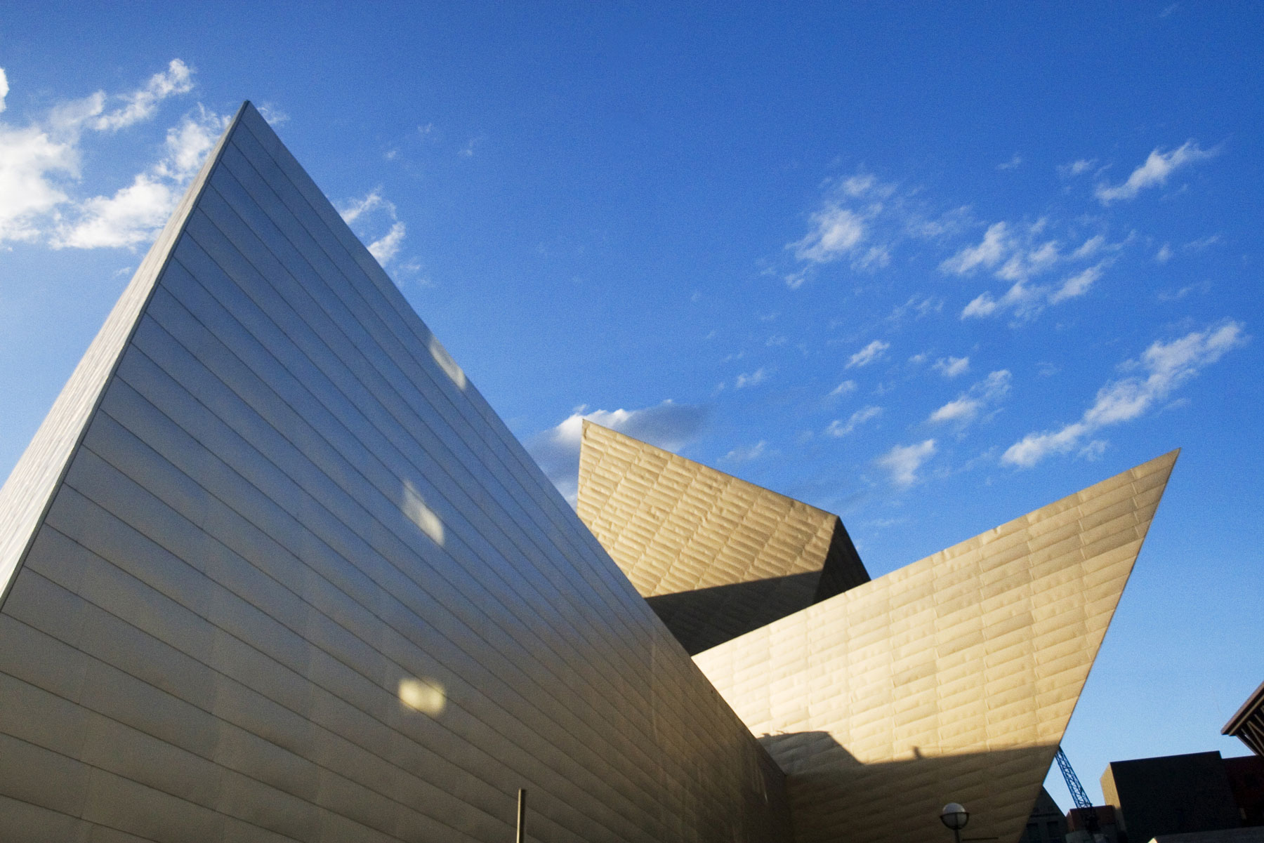 The pointed, metallic, triangle-like shapes of the Denver Art Museum building in Denver, Colorado look like a sculpture against the blue sky.