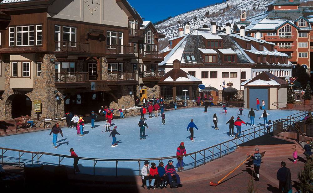 An ice rink with 20 or so skaters sits in the middle of a Bavarian-style village