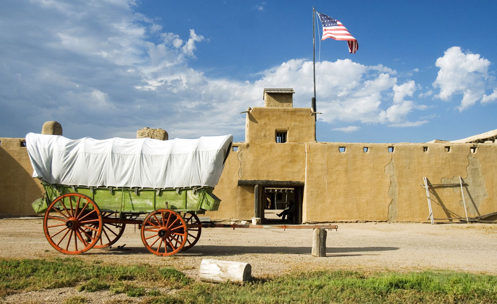 An old fashioned chuckwagon is stopped in front of a large, sand colored building at Bent's Old Fort National Historic Site near La Junta, CO