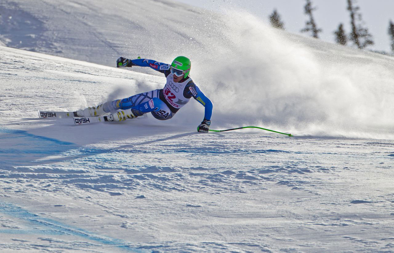 A competitive ski athlete wears a neon green helmet and stirs up fresh snowy powder as they race down the white mountain slope at Beaver Creek Resort in Colorado.