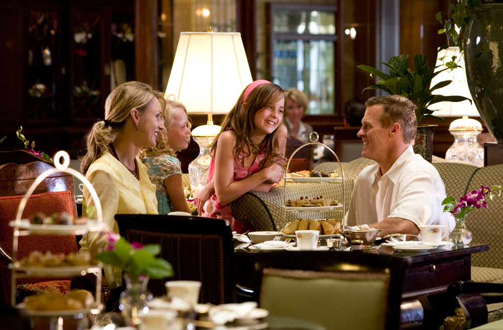 A smiling family enjoys afternoon tea inside a cozy hotel restaurant