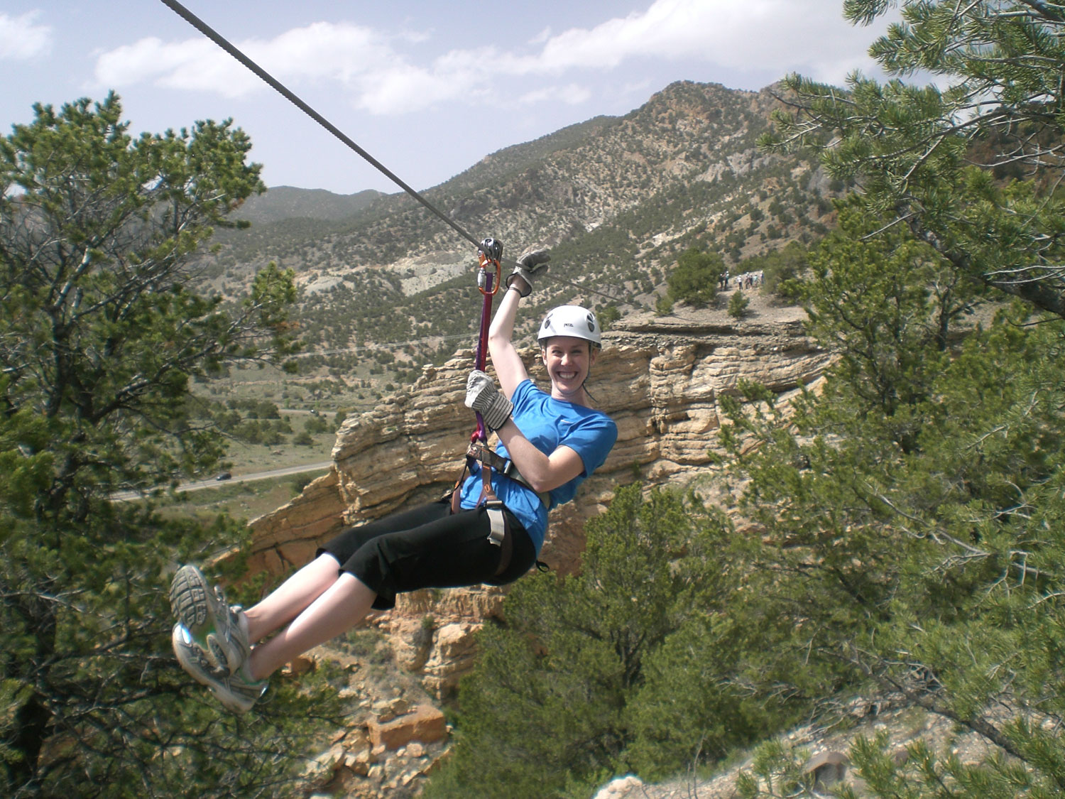 An adventurer in a blue shirt and black pants smiles and whizzes down a zipline in Salida, Colorado.